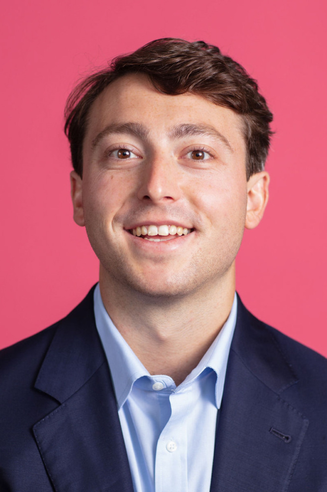 A man smiling in front of a pink background.